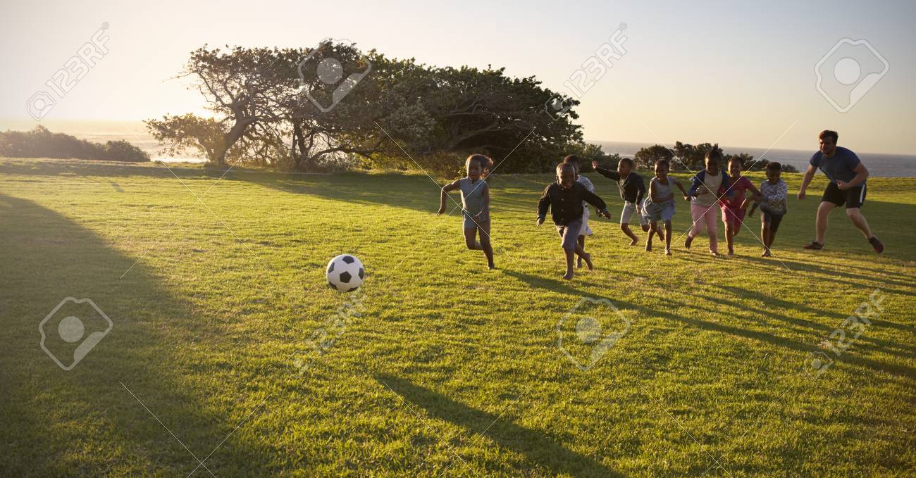 teacher and elementary school kids play football in a field